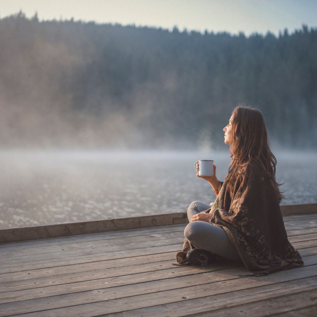 woman enjoyin a cup of gratitude ritual superfood blend sitting on a deck by a lake expressing gratitude